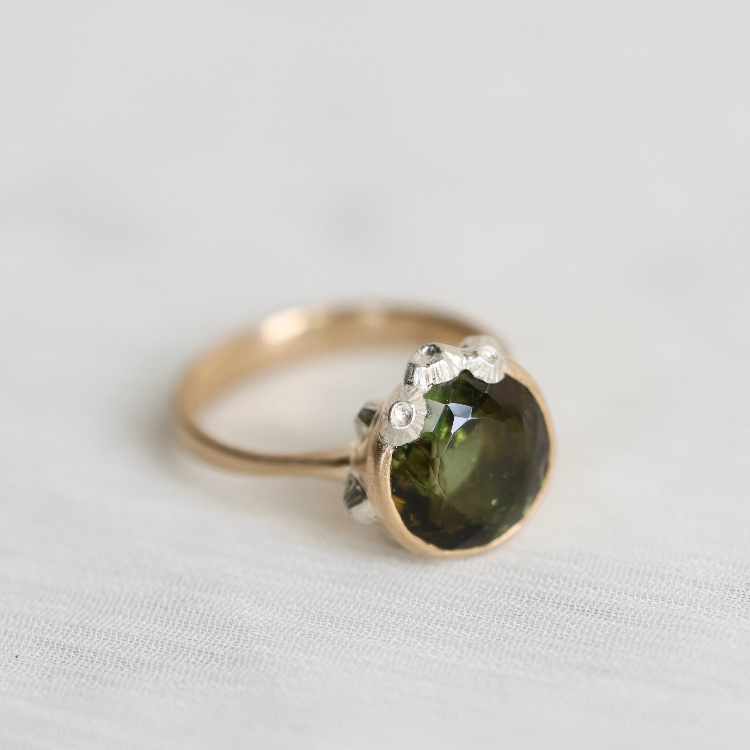 Gold ring with a green gemstone on a light gray background