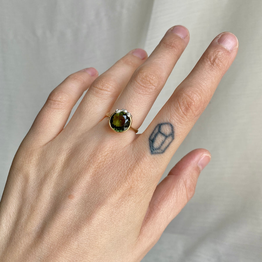 Hand wearing a ring with a green gemstone on a neutral background