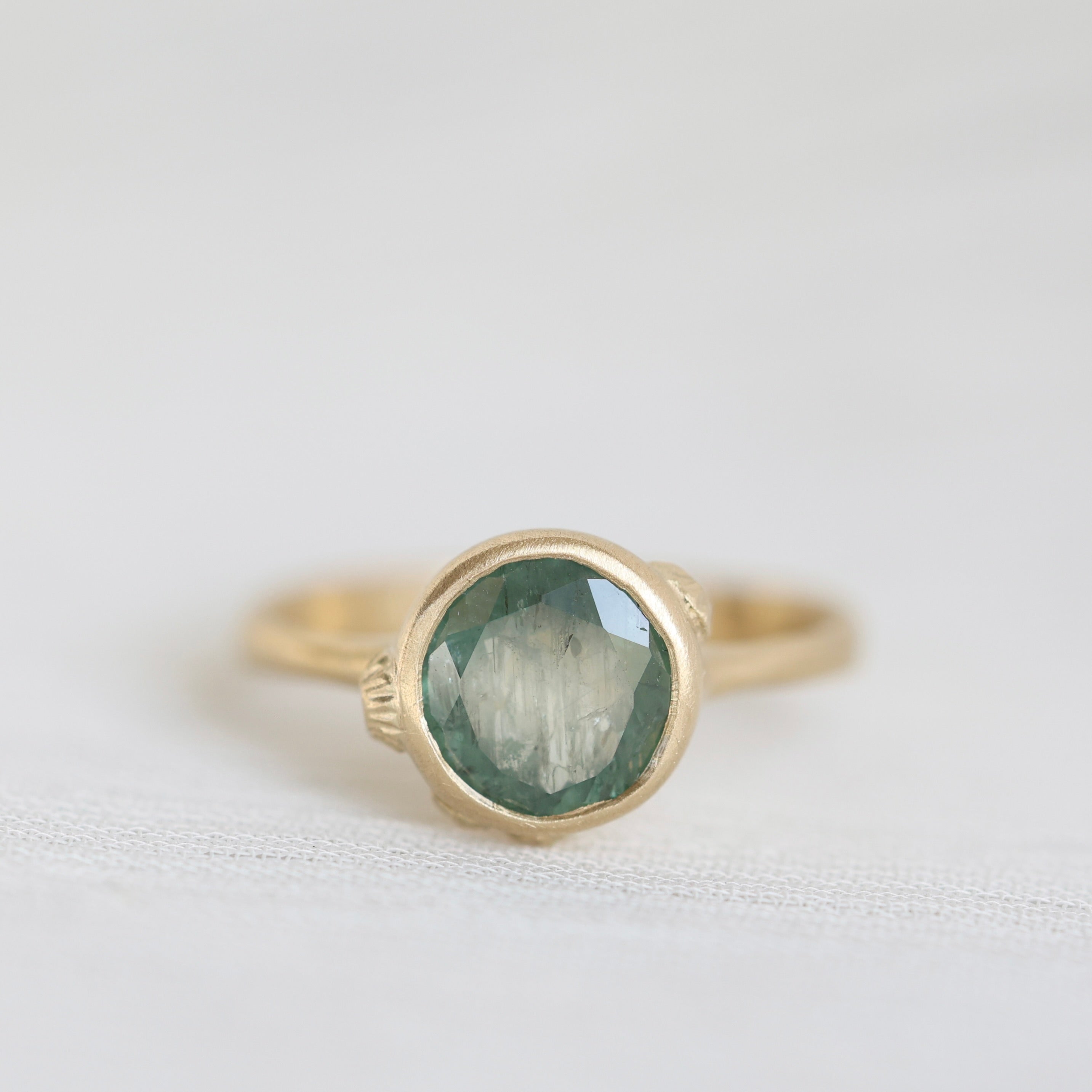 Gold ring with a green gemstone on a light gray background