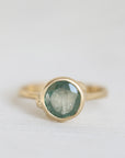 Gold ring with a green gemstone on a light gray background