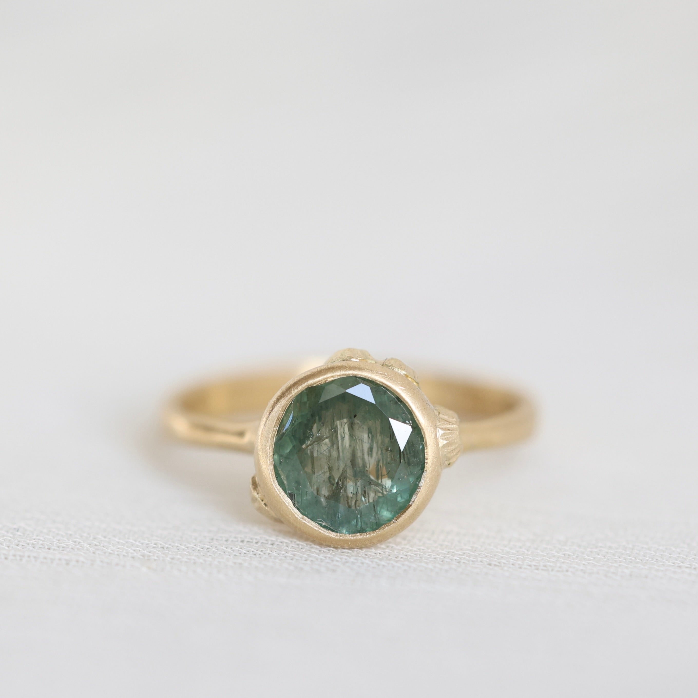 Gold ring with a green gemstone on a light gray background