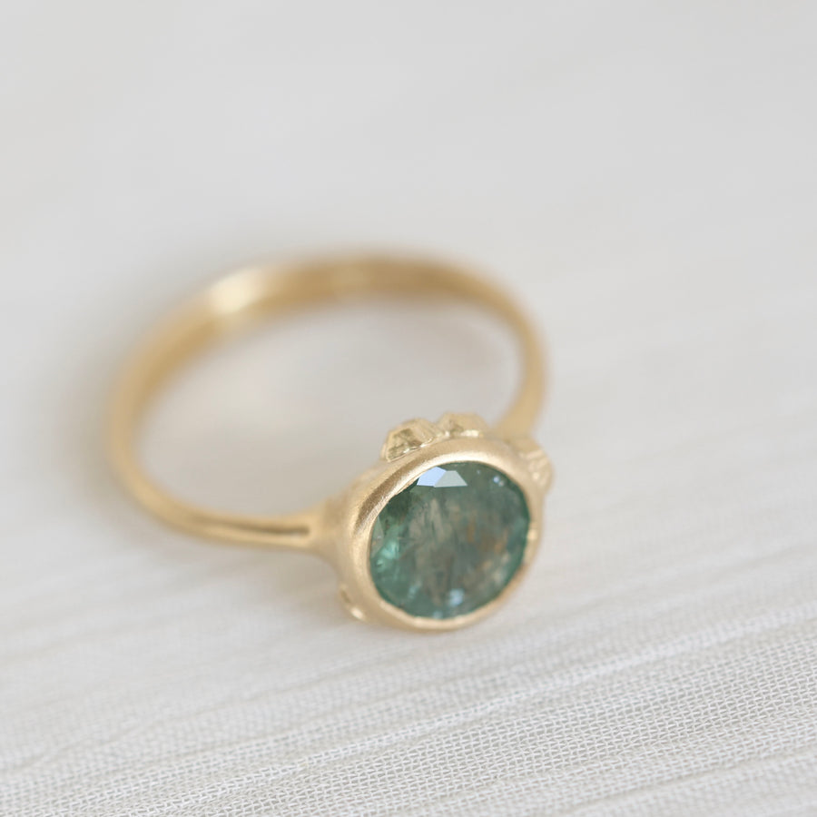 Gold ring with a green gemstone on a light fabric background