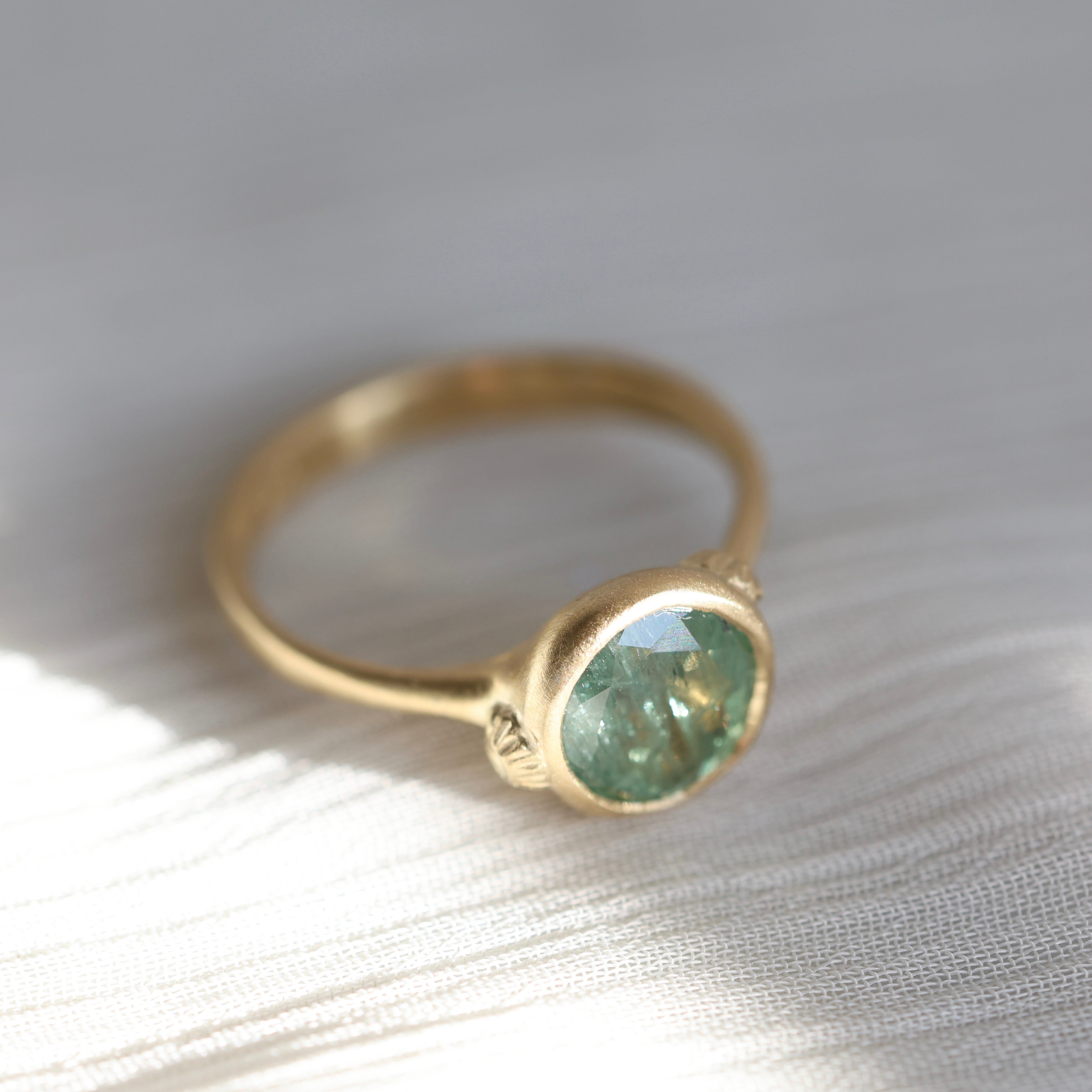 Gold ring with a green gemstone on a textured white surface