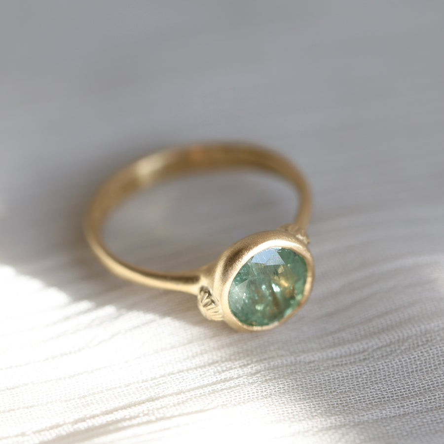 Gold ring with a green gemstone on a textured white surface