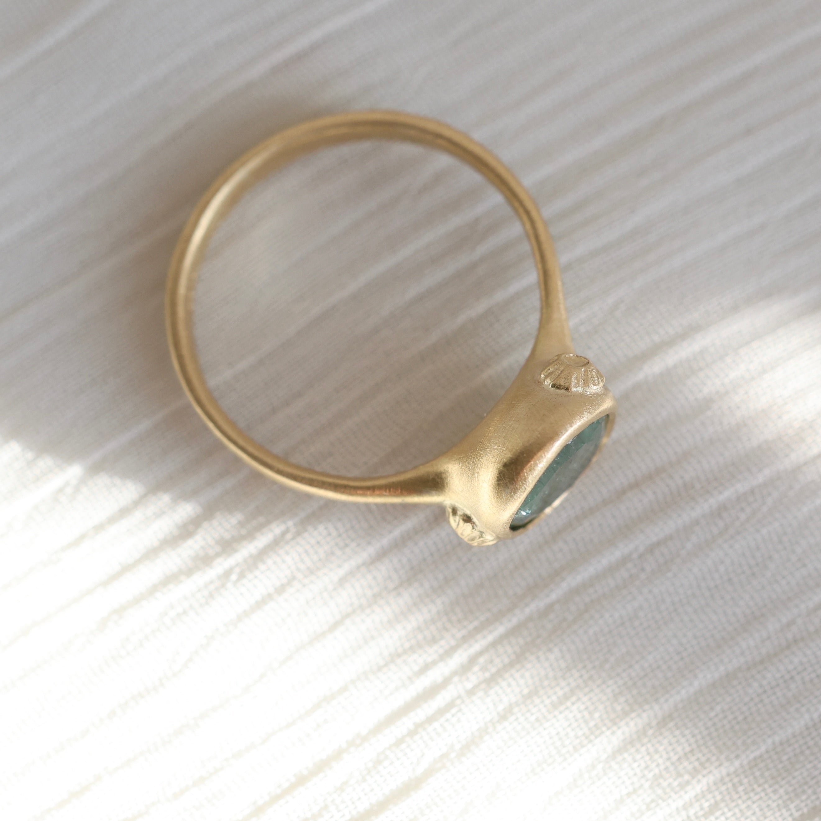 Gold ring with a green gemstone on a textured white surface