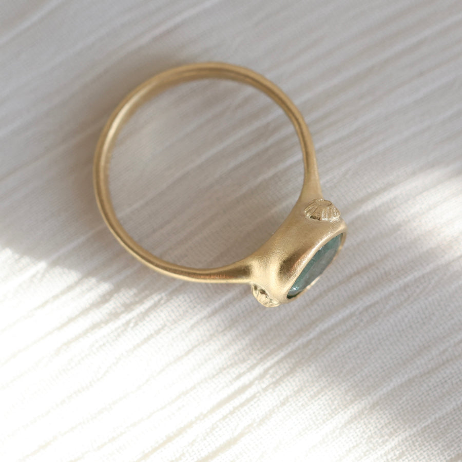 Gold ring with a green gemstone on a textured white surface