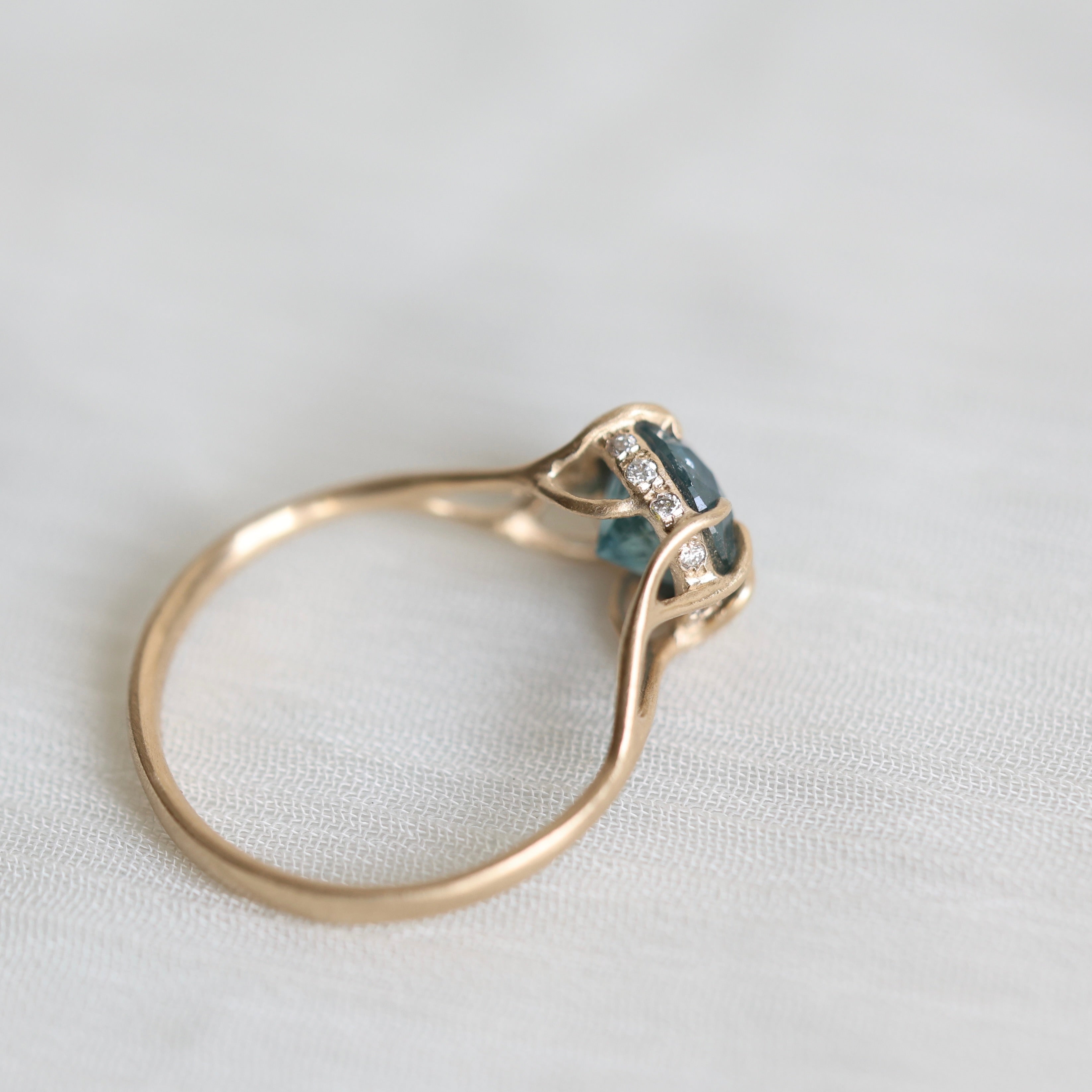 Gold ring with blue gemstone and diamonds on a light fabric background