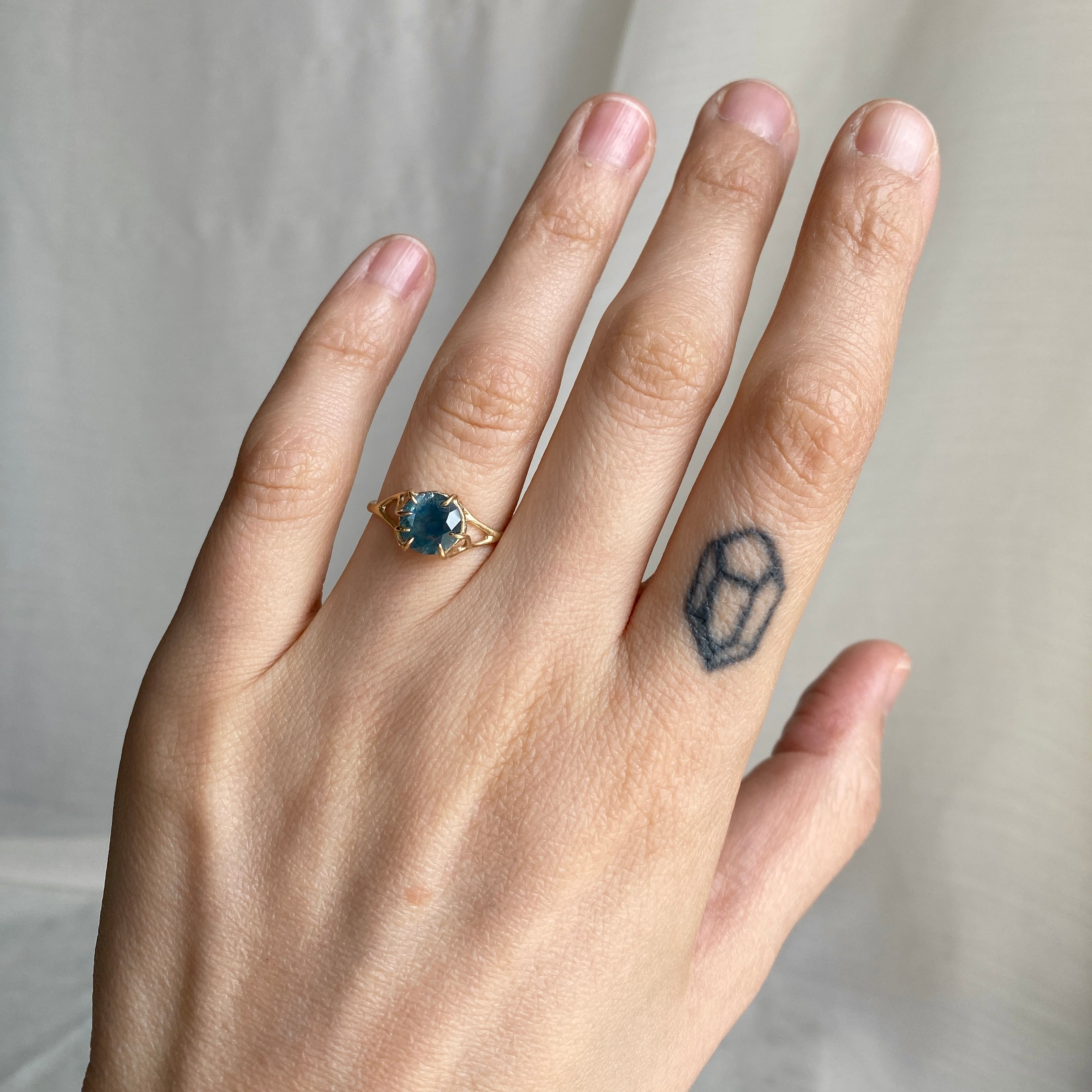 Hand wearing a gold ring with a blue gemstone on a neutral background