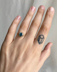 Hand wearing a gold ring with a blue gemstone on a neutral background