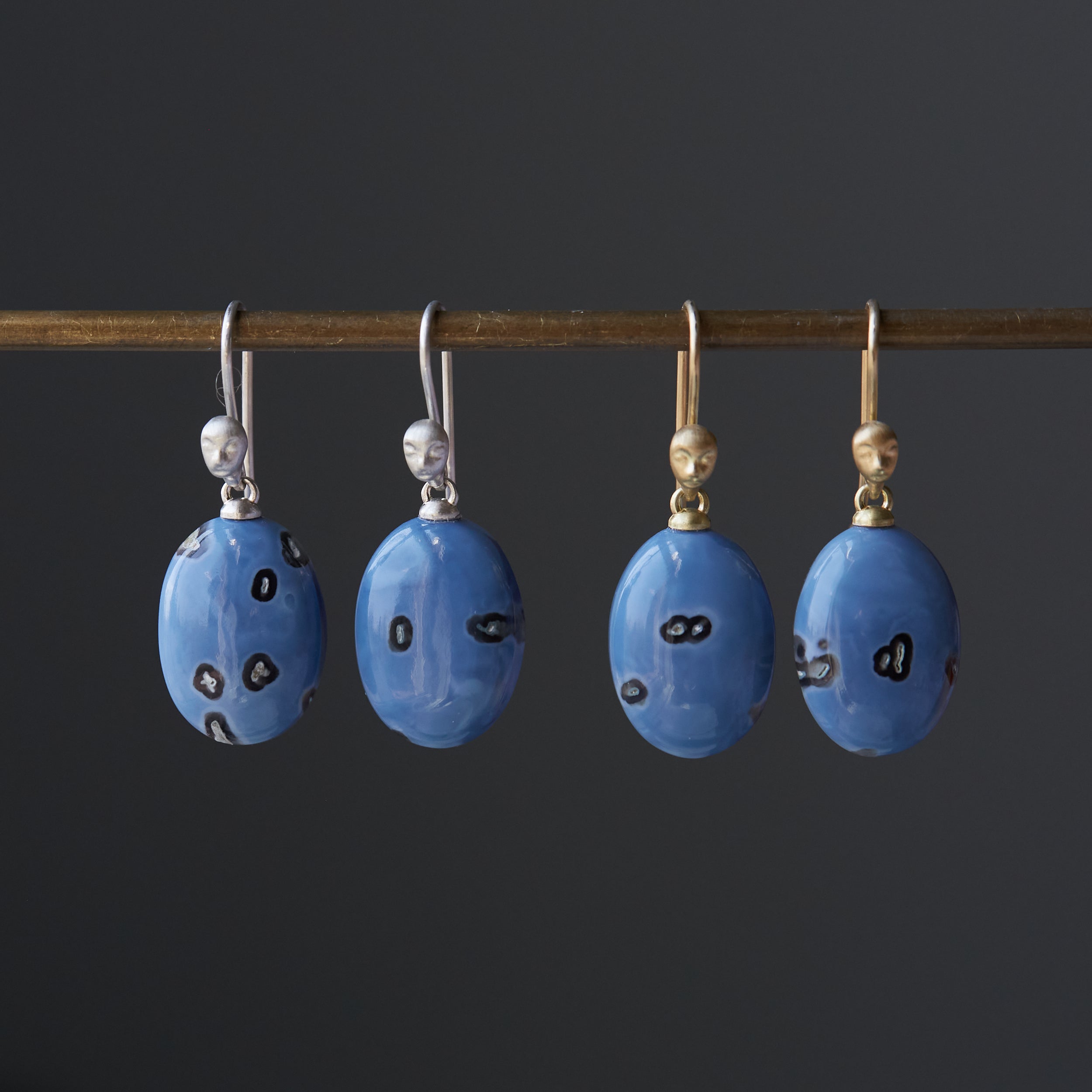two pairs of periwinkle blue common opal with mottled black spots. One pair is silver, the other in gold. Little Lady faces adorn the ear wires.