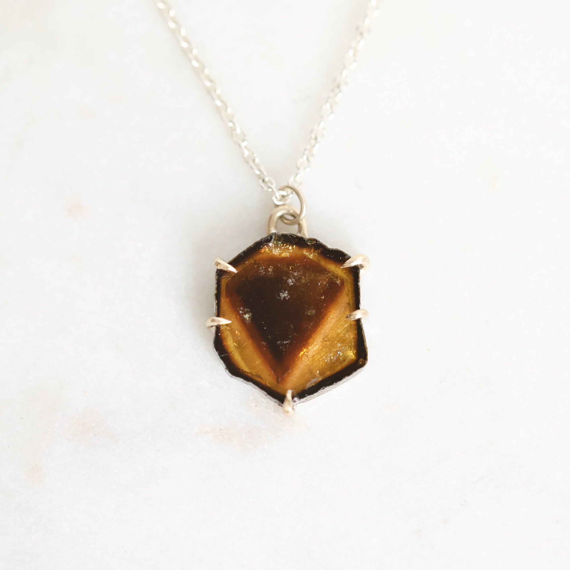 A silver necklace with a hexagonal pendant featuring a polished tiger's eye stone, displayed on a clean white background.