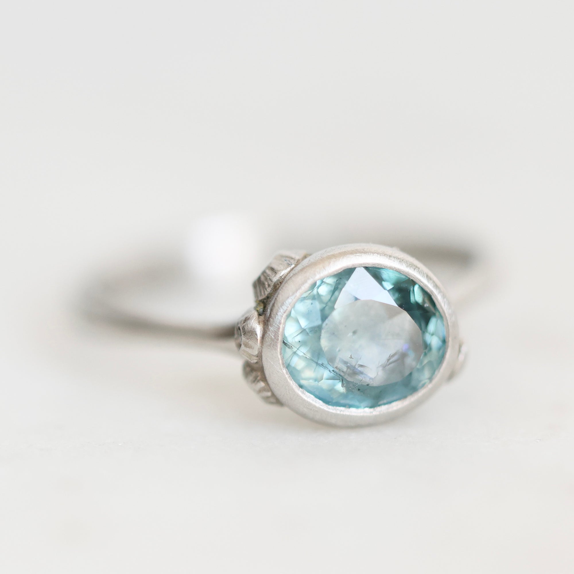 A silver ring featuring an oval-cut light blue gemstone, photographed on a clean, light gray background.