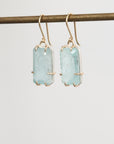 Pair of earrings with light blue gemstones on a thin rod against a white background