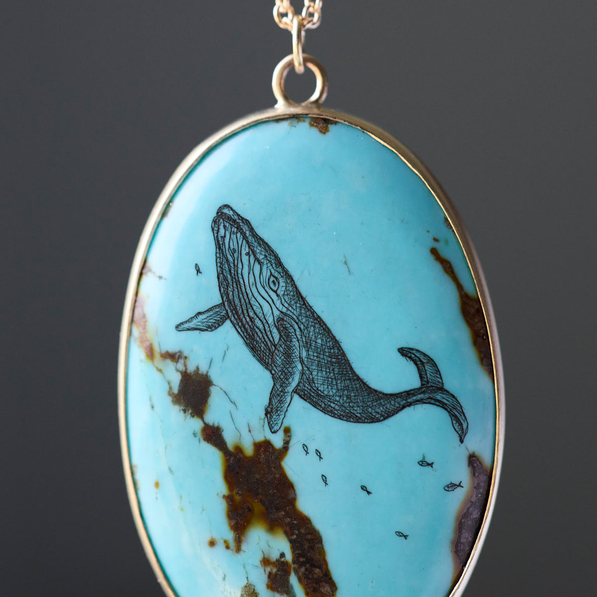 An oval pendant necklace featuring a light blue turquoise stone with natural brown matrix and a detailed black whale illustration, set in a gold-tone bezel with a matching chain.