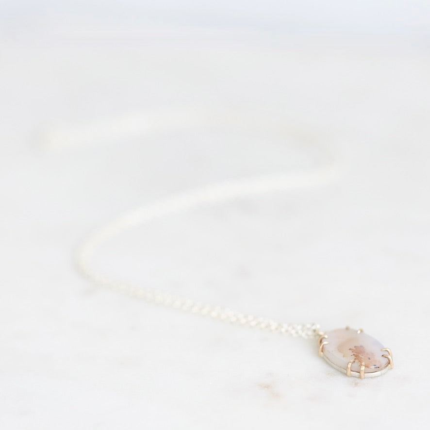dendritic agate necklace laying on white surface