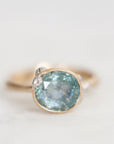 A gold ring featuring a large oval light blue gemstone with tiny inclusions, accented by small clear stones on either side, set against a soft white background.