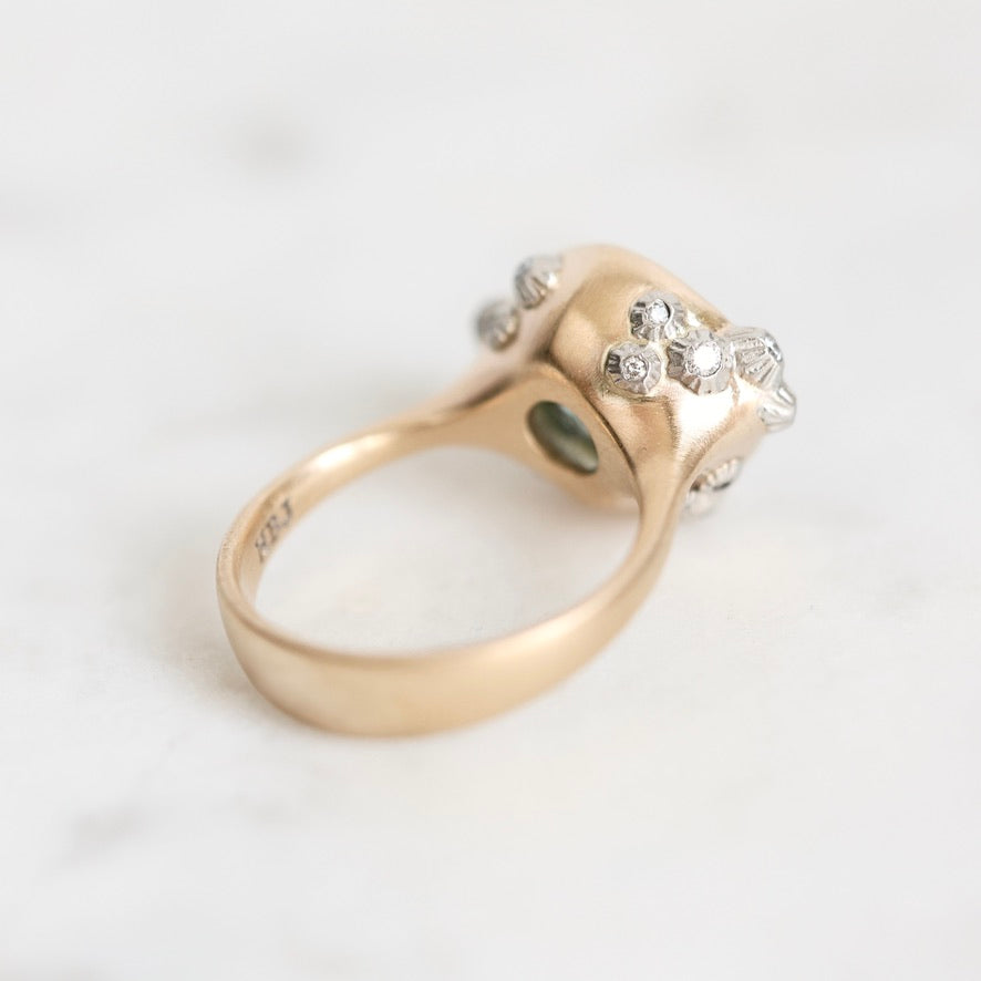 A vintage-style ring with a polished yellow gold band and a cluster of small clear gemstones on a light marble surface.