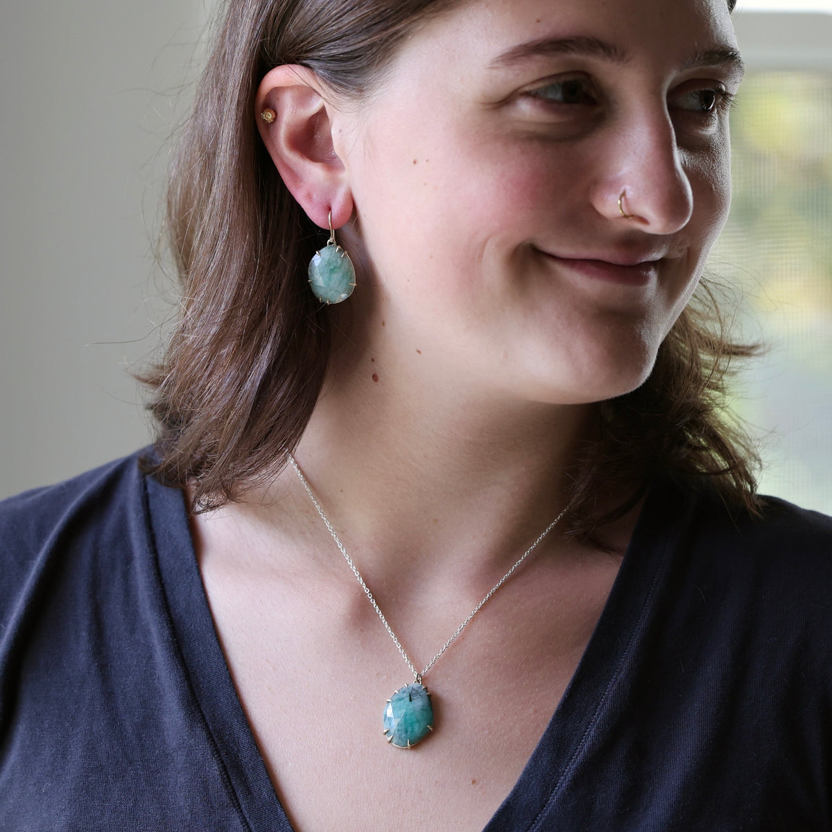A woman wearing a silver necklace with a turquoise-colored oval pendant and matching drop earrings, shown in a close-up portrait.