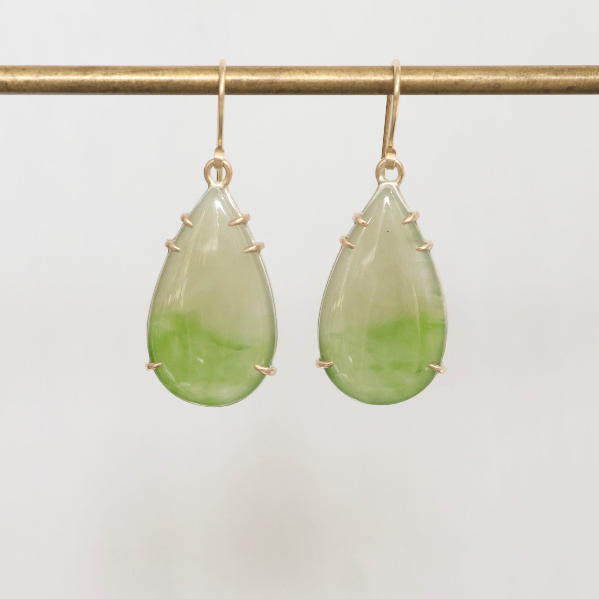 Teardrop-shaped green earrings on a gold hook against a light gray background