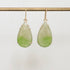 Teardrop-shaped green earrings on a gold hook against a light gray background