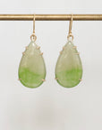 Teardrop-shaped green earrings on a gold hook against a light gray background