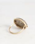A gold ring with a textured, silver-toned oval face, photographed on a clean white surface.