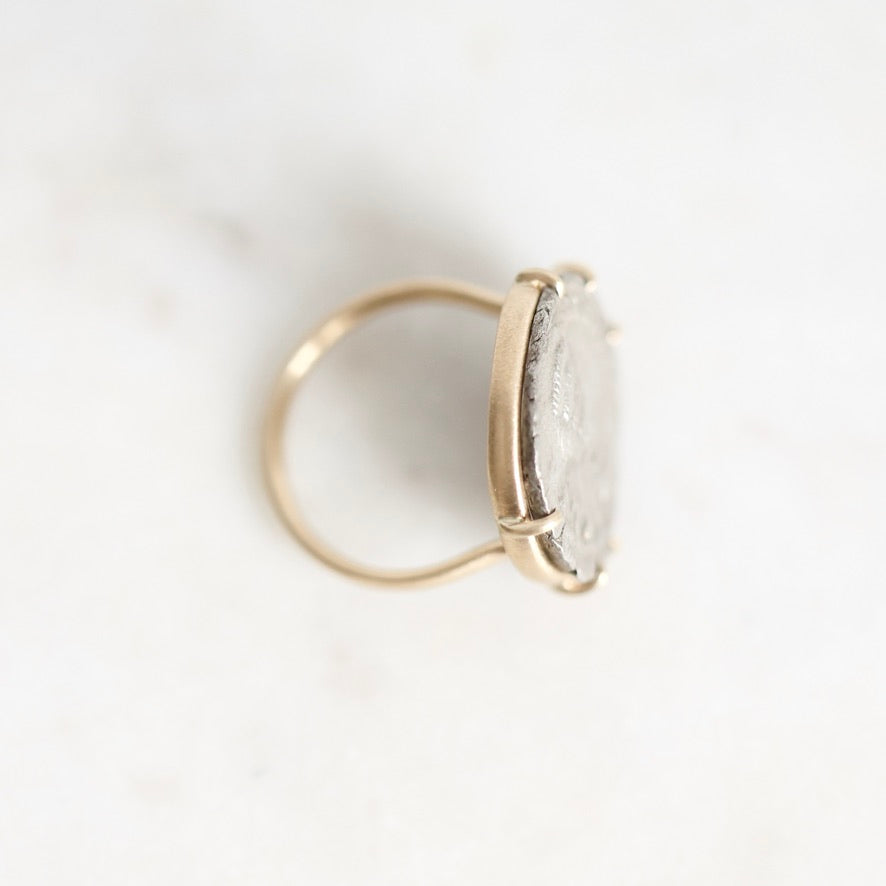 A gold ring with a large, oval, clear stone set in a prong setting, photographed on a light marble surface.