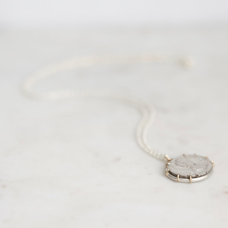 A silver necklace with a round pendant featuring a textured, frosted white stone, resting on a light marble surface.