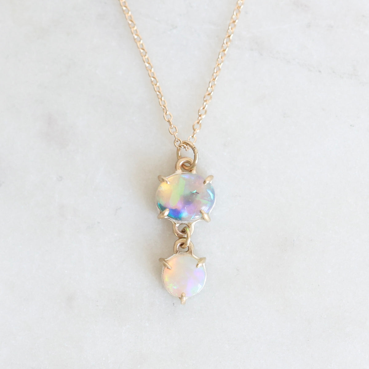 Two stone opal pendant set in yellow gold with a yellow gold chain against a neutral background. 