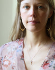 Woman wearing double stone opal necklace. She is wearing large gold hoops and a floral blouse against an indoor background. 