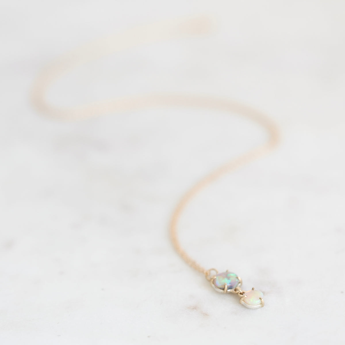 Two stone opal necklace set ing gold with a gold chain laying on a marble background.