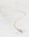 Two stone opal necklace set ing gold with a gold chain laying on a marble background.