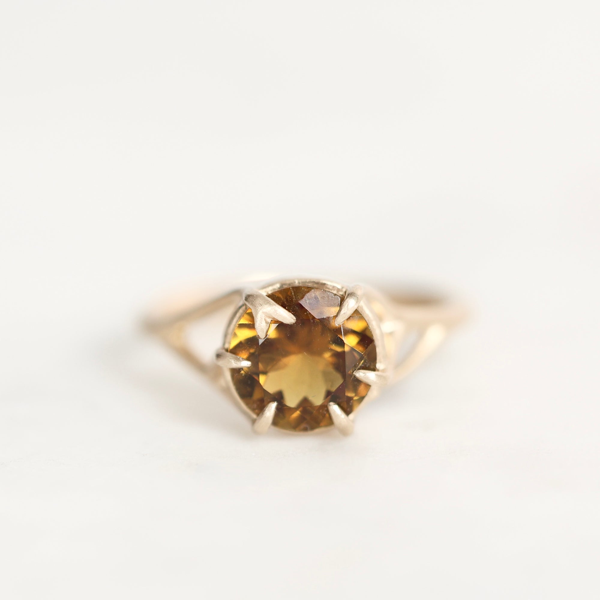 A yellow gold ring featuring a round-cut brown gemstone in a prong setting, photographed against a plain white background.