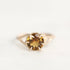A yellow gold ring featuring a round-cut brown gemstone in a prong setting, photographed against a plain white background.
