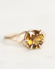 A yellow gold ring with a round-cut gemstone in a prong branch setting, shown on a plain white background.