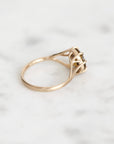 A gold ring with a unique branch band and a small central stone, resting on a light marble surface.