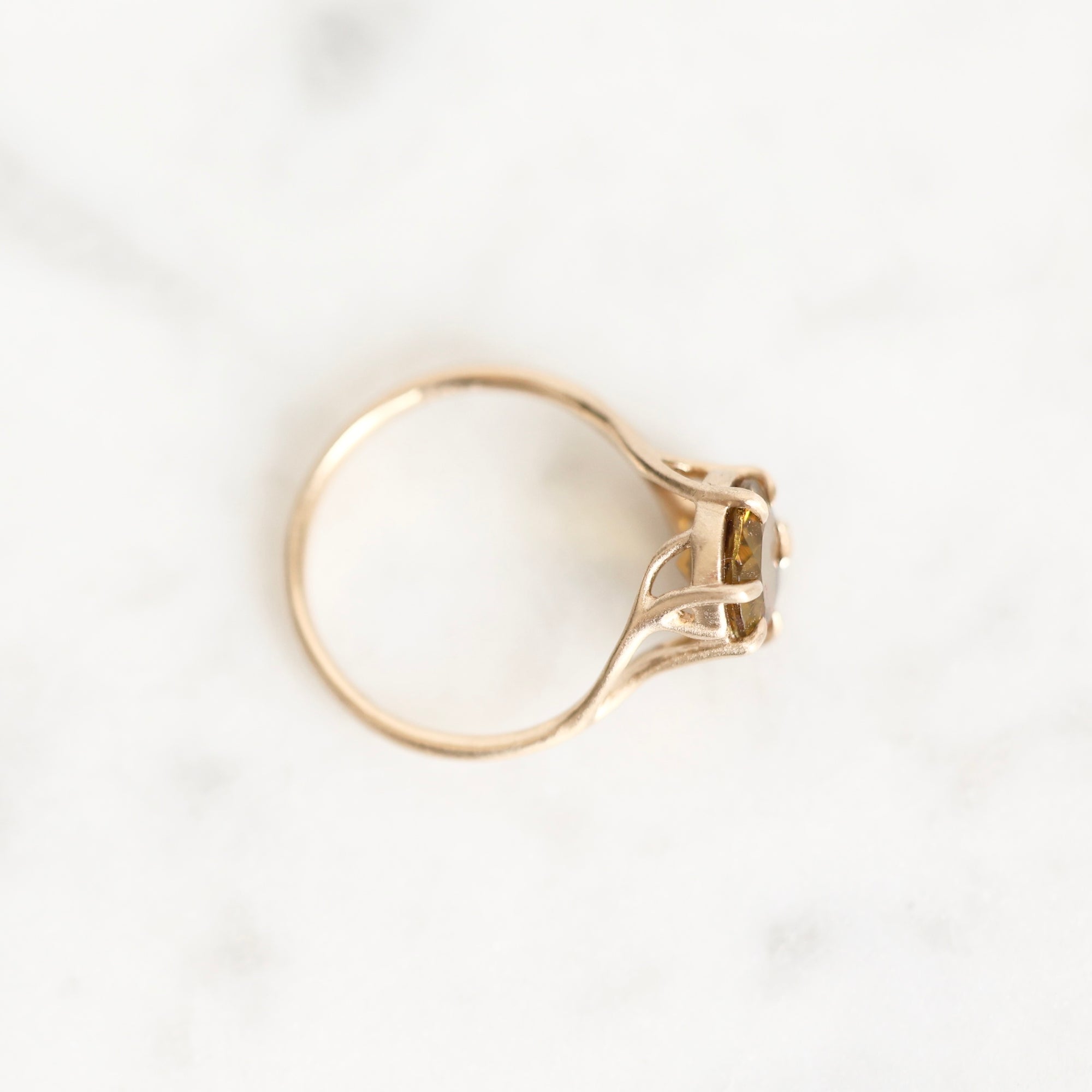 A gold ring with a small central stone, photographed from above on a light marble surface.