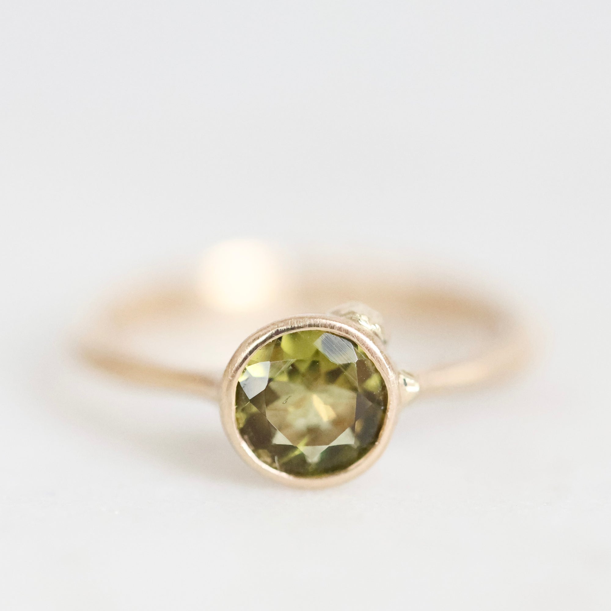 A gold ring with a round faceted olive green gemstone in a prong setting, photographed against a clean white background.