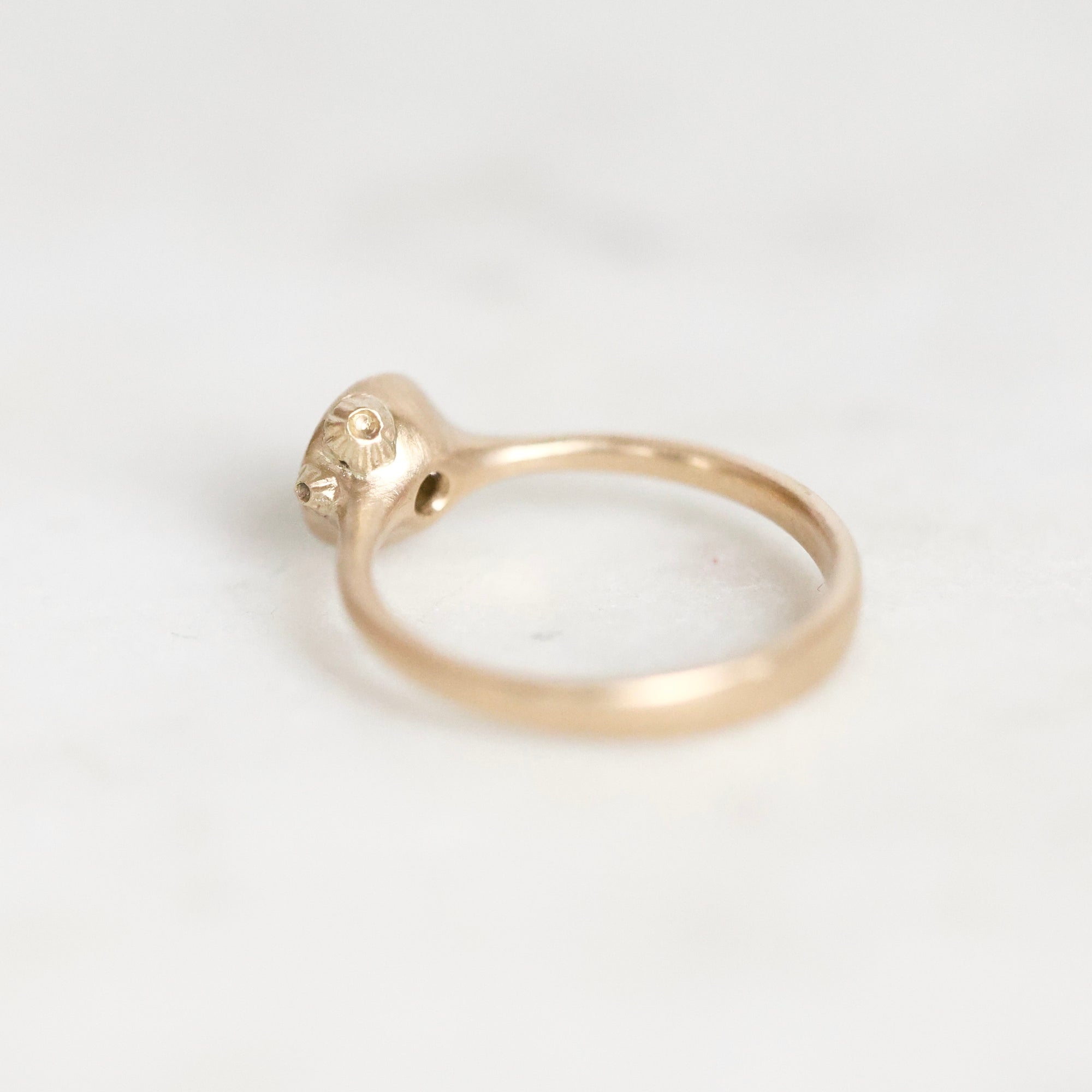 A gold ring with a textured, organic-shaped bezel holding a small gemstone, photographed on a light gray background.