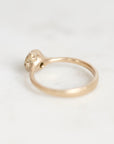 A gold ring with a textured, organic-shaped bezel holding a small gemstone, photographed on a light gray background.