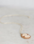 A delicate gold necklace with a cream-colored carved cameo pendant, resting on a light marble surface.
