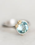 Platinum bezel set ring with aquamarine surrounded by gold barnacles.