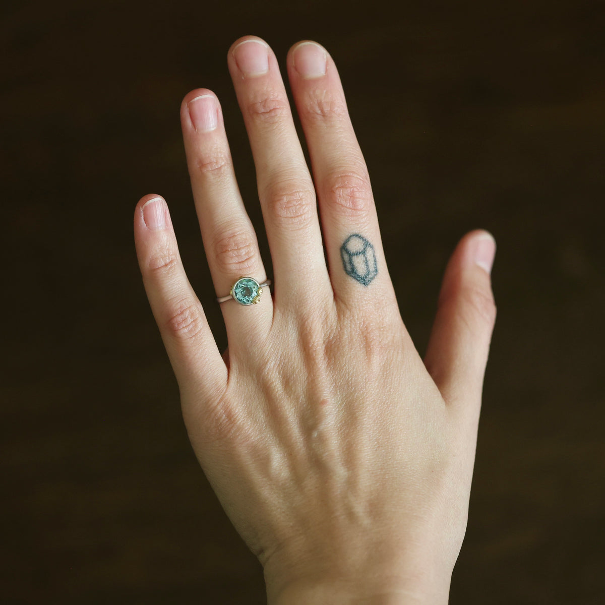 Hand wearing aquamarine bezel set with gold barnacles. 