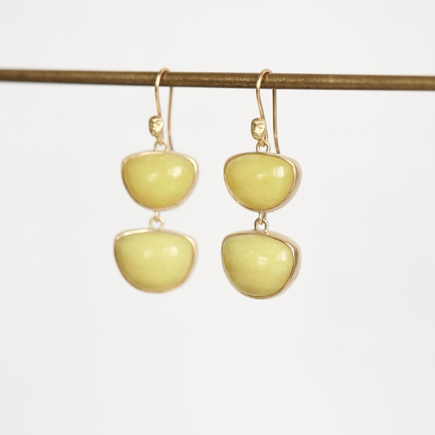 A pair of gold drop earrings with two smooth, pale yellow stone-like oval shapes, hanging from a thin horizontal gold rod against a plain white background.