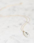 A delicate gold chain necklace with a small, teardrop-shaped white pendant featuring a black lighthouse engraving, displayed on a light marble surface.