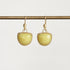 A pair of gold drop earrings with smooth, dome-shaped pale yellow-green stones, hanging from a gold horizontal bar against a light gray background.