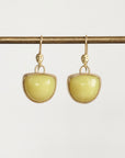 A pair of gold drop earrings with smooth, dome-shaped pale yellow-green stones, hanging from a gold horizontal bar against a light gray background.