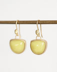 A pair of gold drop earrings with smooth, rounded pale yellow-green stone pendants, hanging from a thin horizontal gold rod against a plain white background.
