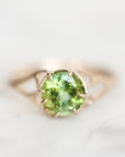 A rose gold ring featuring a round-cut green peridot gemstone in a prong setting, resting on a light marble surface.