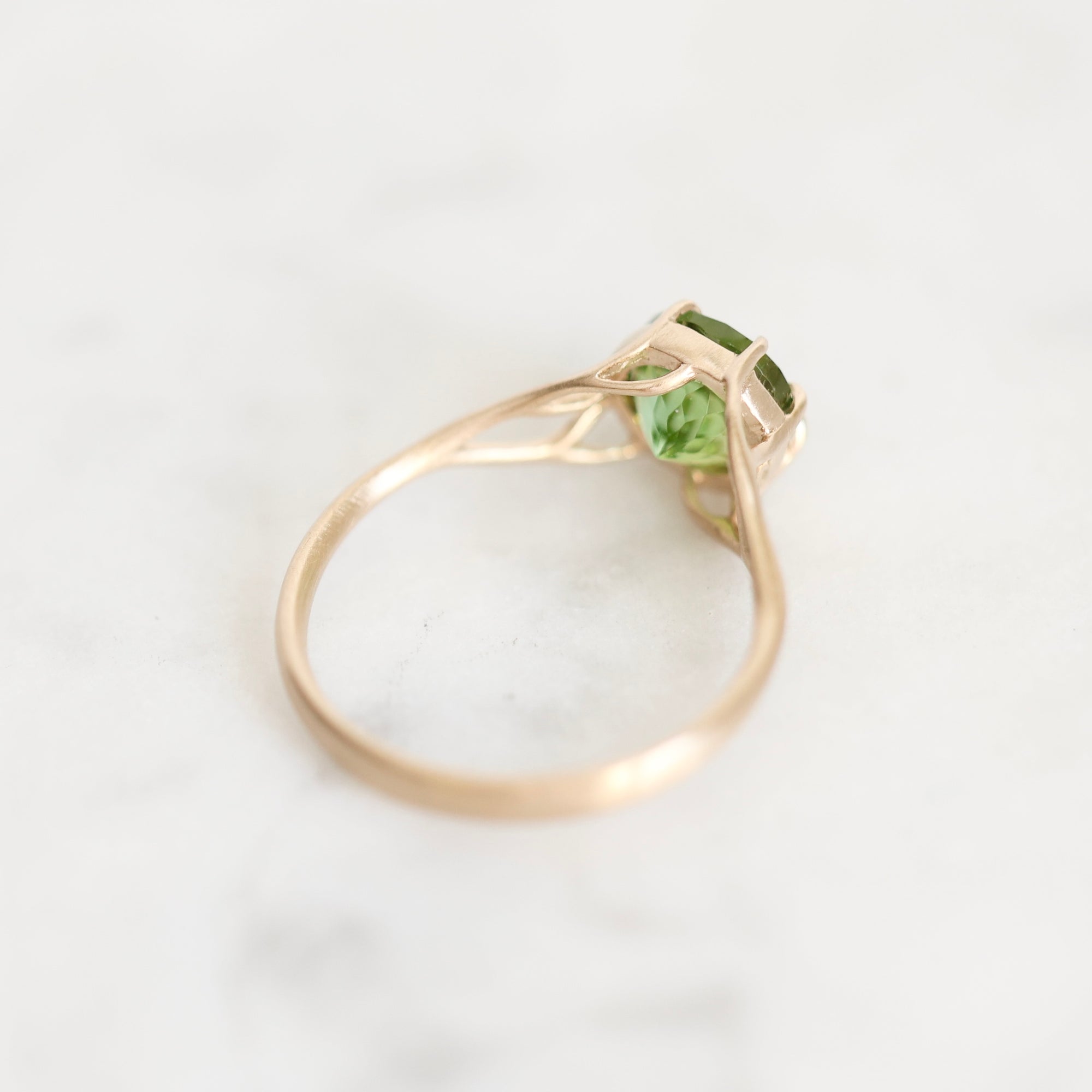 A rose gold ring with a green gemstone, photographed on a light marble surface.